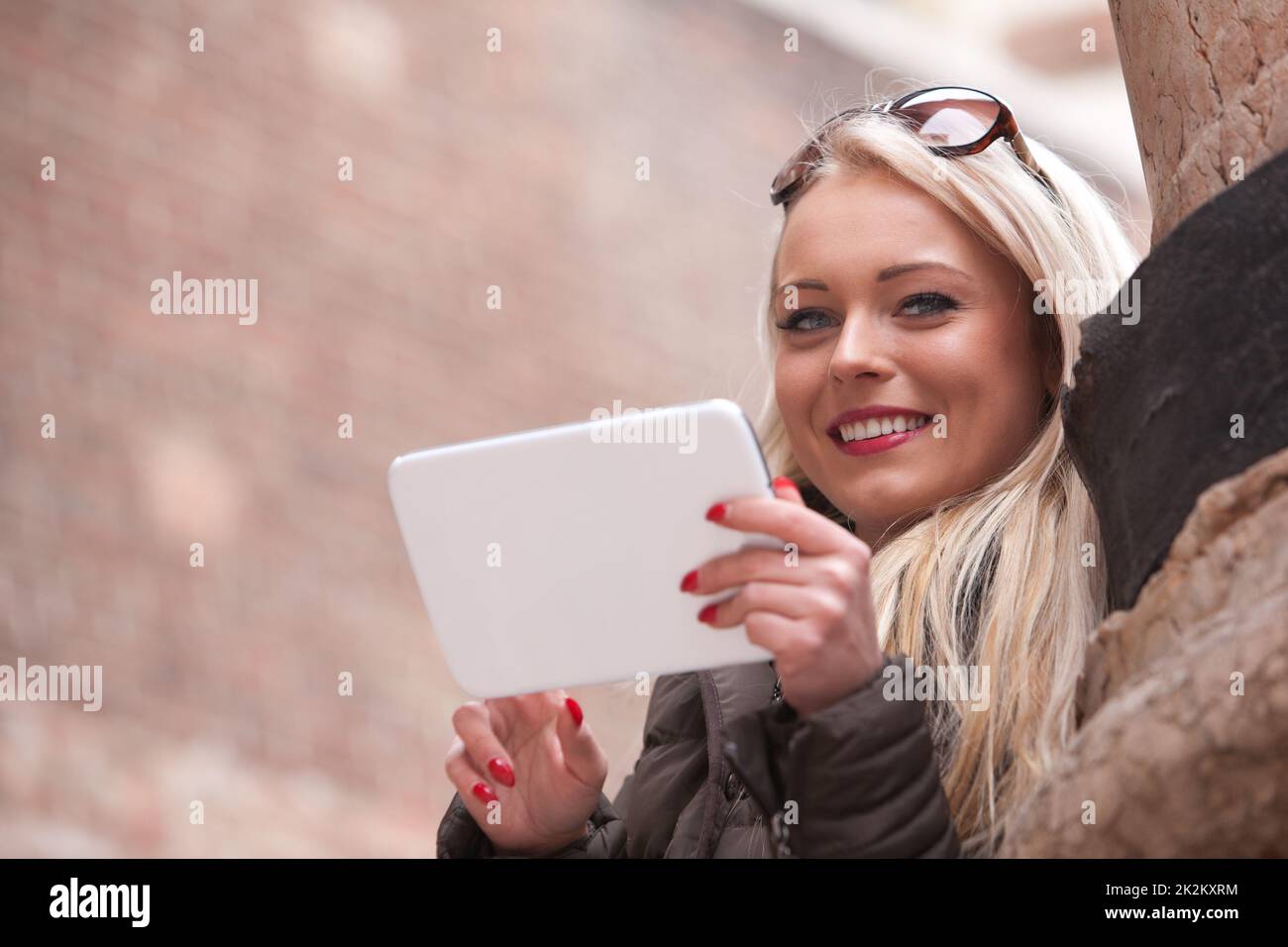 Blondes lächelndes Mädchen mit einem Tablet im Freien Stockfoto