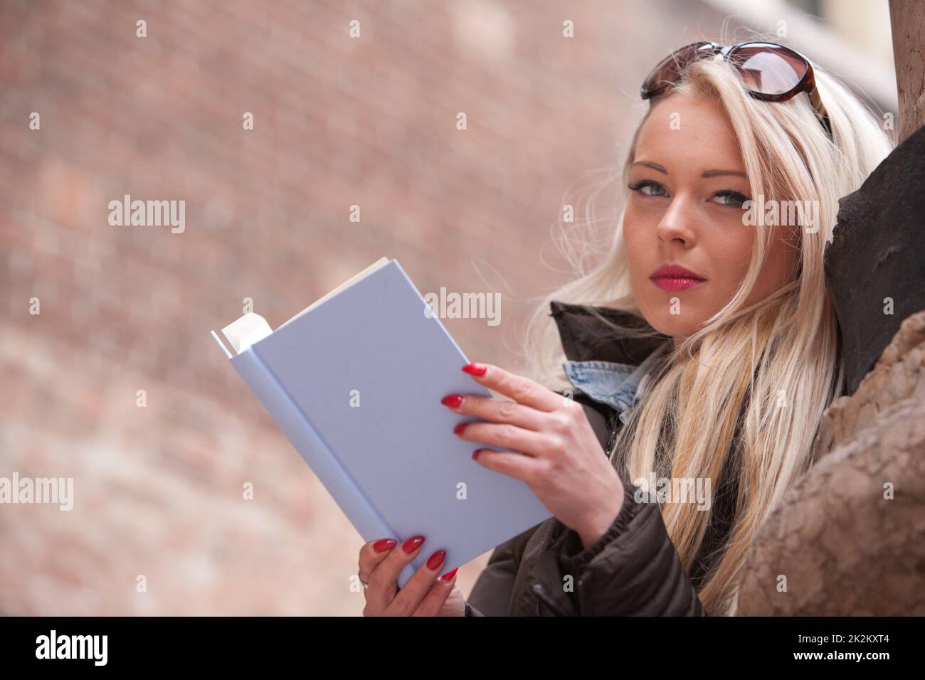 Blonde junge Frau, die draußen ein Buch liest Stockfoto