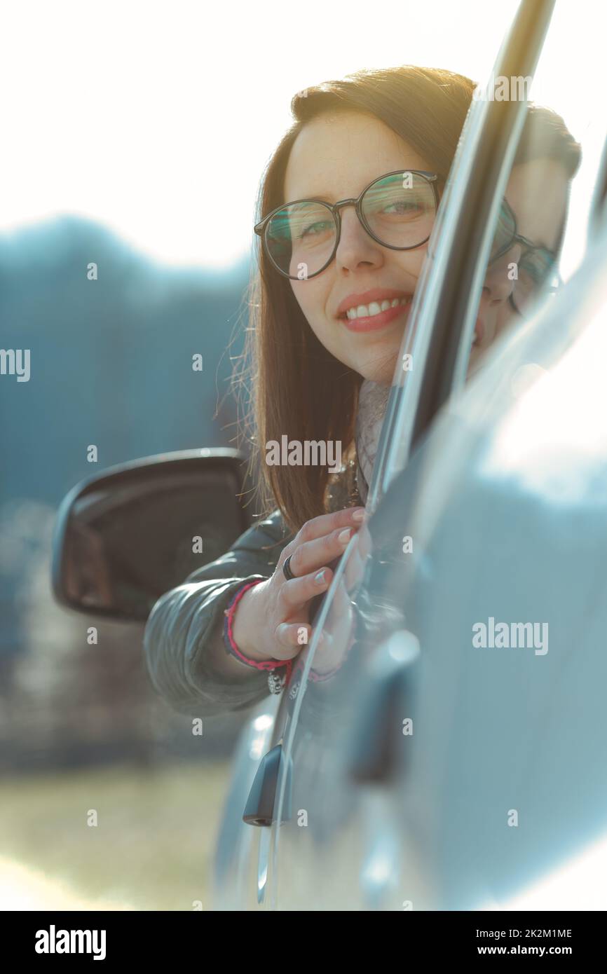 Lächelnde Frau, die sich aus einem Auto lehnt und zurückblickt Stockfoto