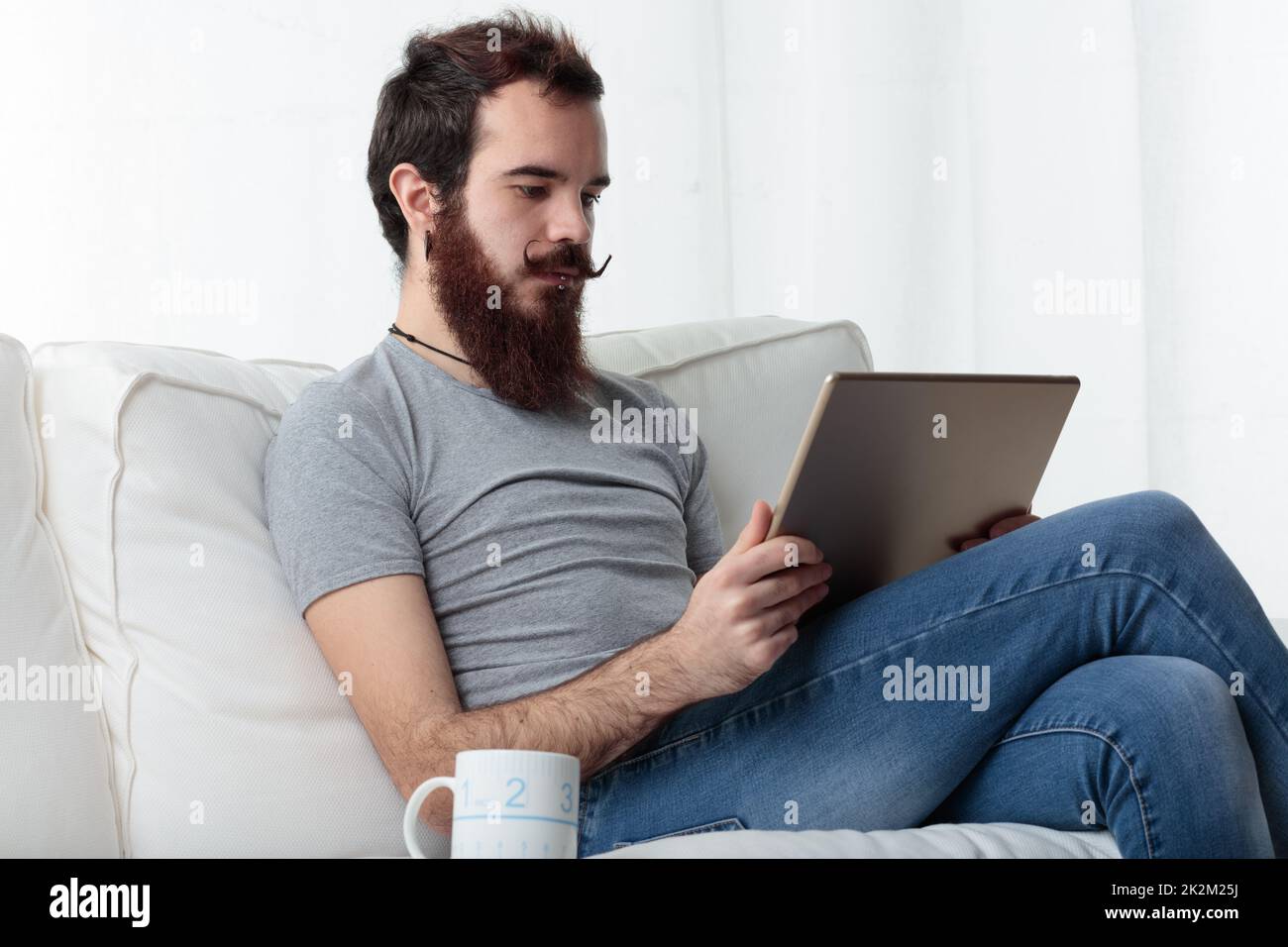Mann mit Bart und Schnurrbart entspannt mit einem digitalen Tablet Stockfoto