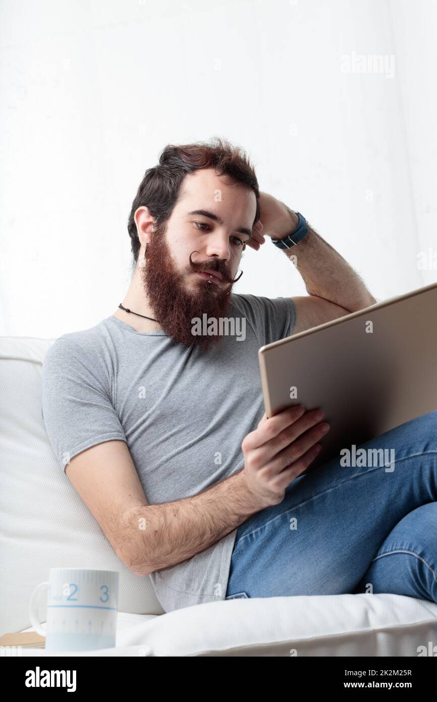 Mann mit Bart und Schnurrbart entspannt mit einem digitalen Tablet Stockfoto