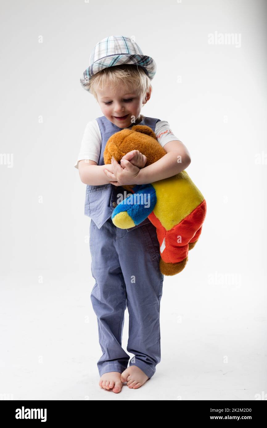 Ein kleines Baby mit Hut, das seinen Teddybär umarmt Stockfoto