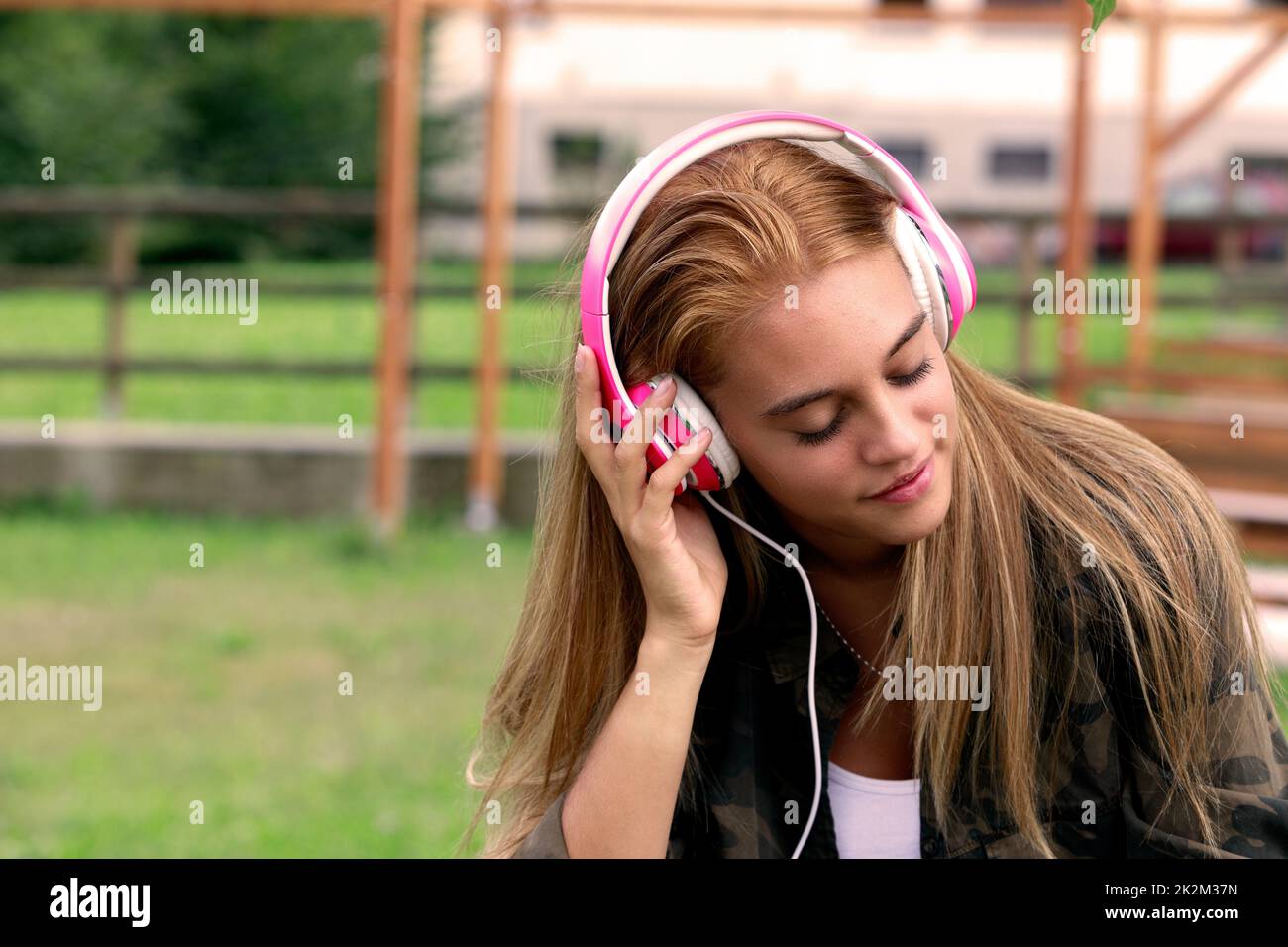 Ein Mädchen mit pinkfarbenen Kopfhörern hört Musik im Park Stockfoto