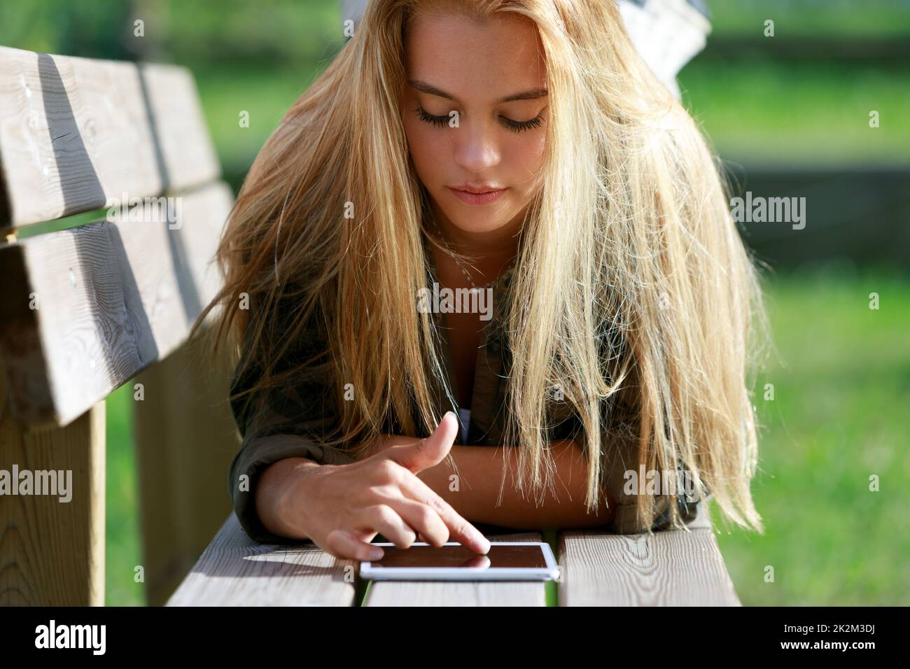 Eine junge Frau, die sich auf einer Bank entspannt und mit ihrem Handy surft Stockfoto