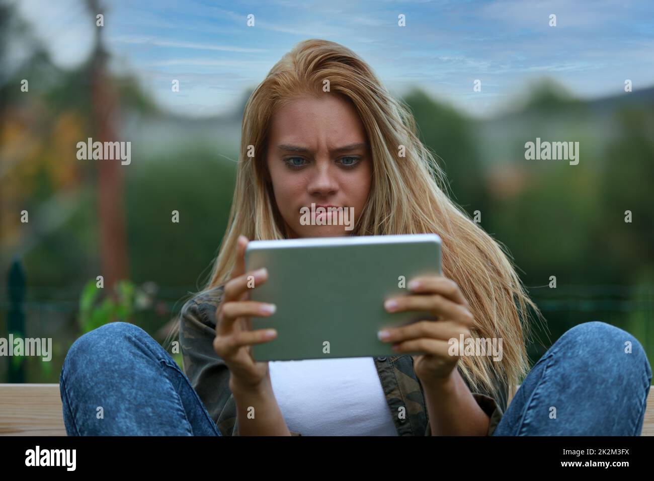 Verwirrte junge Frau, die auf ihre Tafel starrt Stockfoto