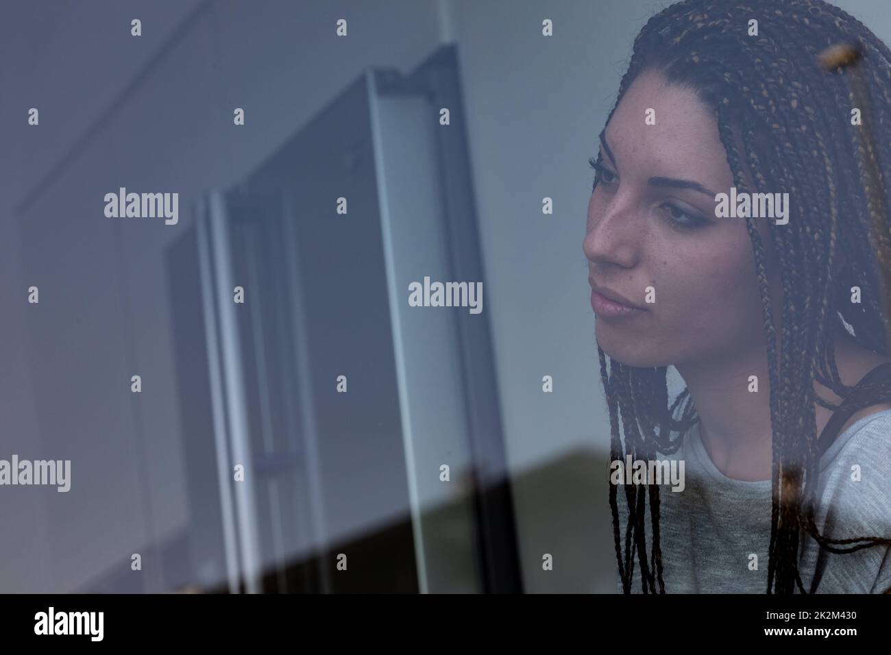 Eine einsame junge Frau, die aus dem Fenster starrt und Sehnsucht hat Stockfoto