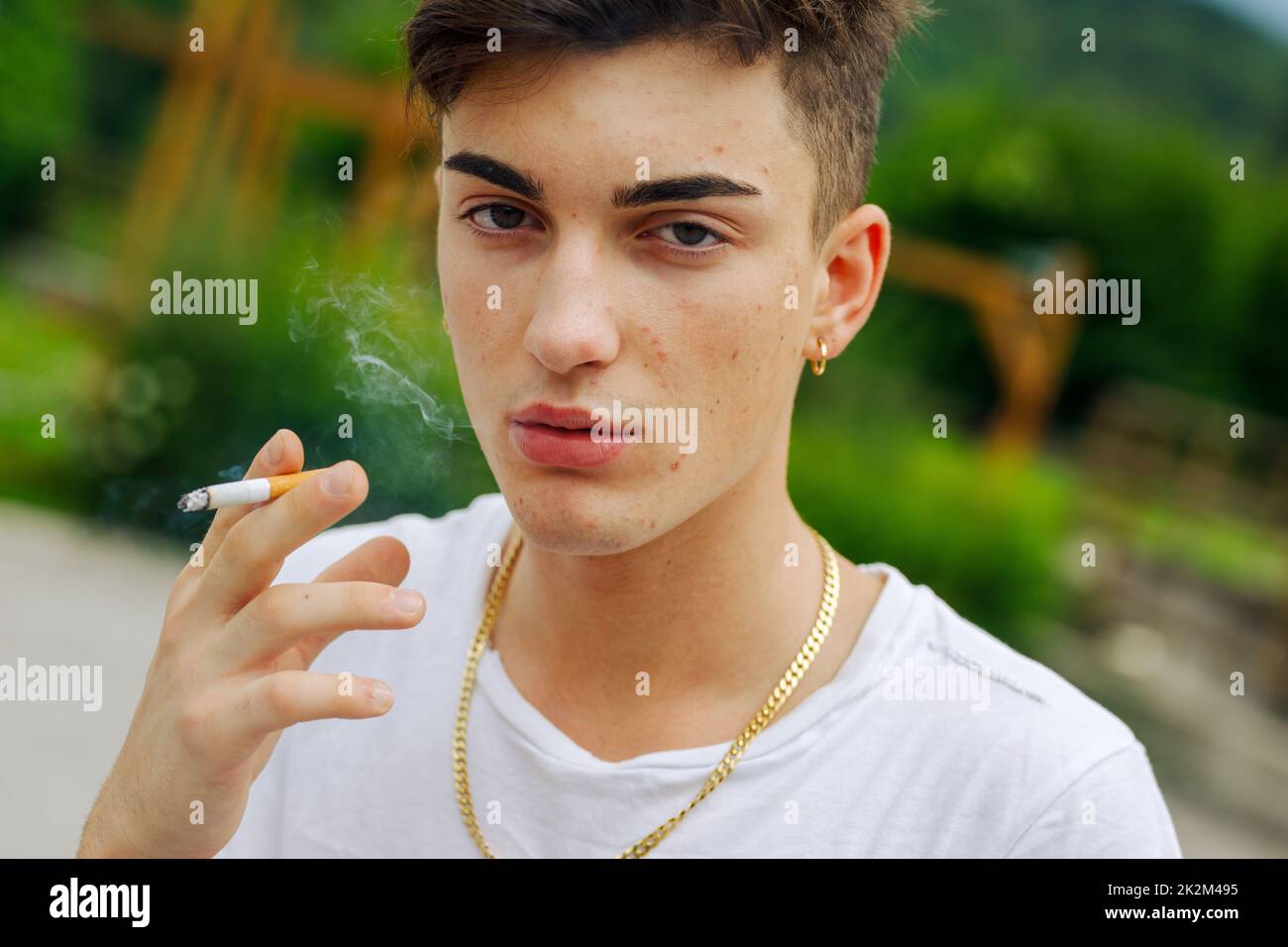 Ein ernster junger Mann raucht draußen eine Zigarette und atmet den Rauch aus Stockfoto