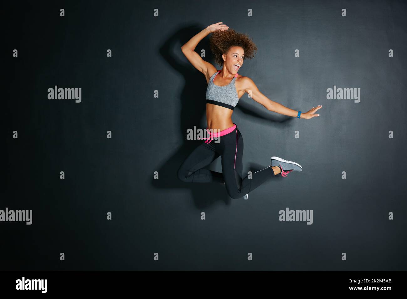 Schauen Sie immer auf die helle Seite des Lebens. Aufnahme einer sportlichen jungen Frau, die vor grauem Hintergrund springt. Stockfoto