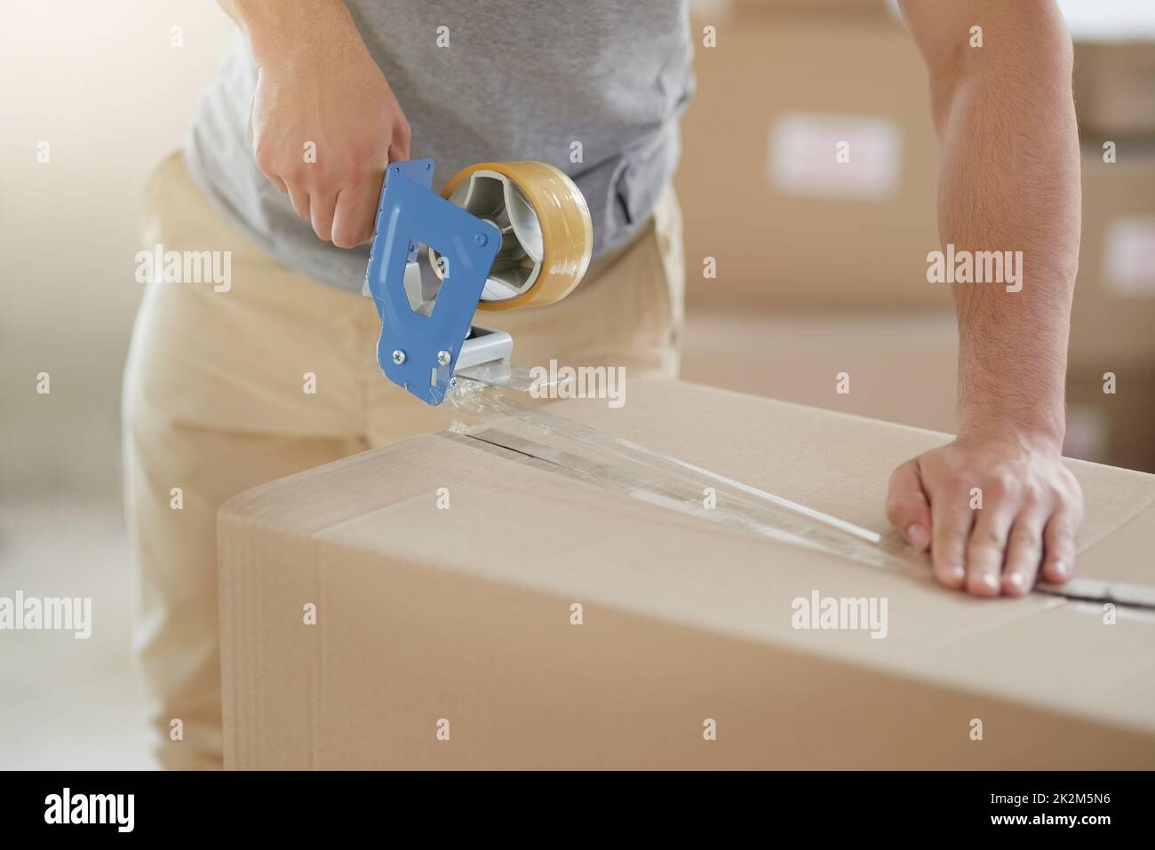 Versiegelt und gesichert. Aufnahme eines nicht identifizierbaren jungen Mannes, der zu Hause einen Karton mit Klebeband schloss. Stockfoto