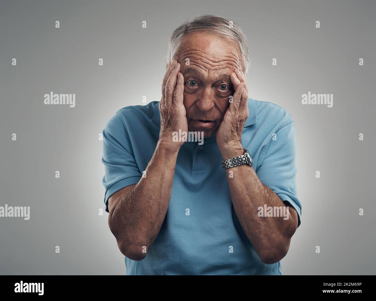 Der Stress könnte mich einfach umbringen. Aufnahme eines älteren Mannes, der in einem Studio vor grauem Hintergrund die Hände an sein Gesicht klammert. Stockfoto