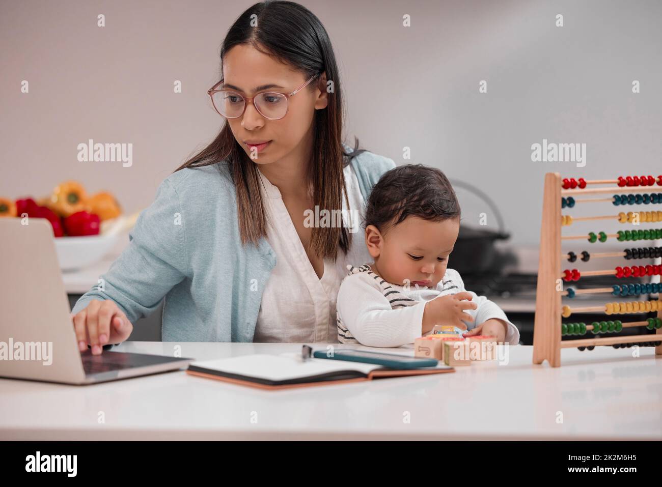 Ich tue alles für euch. Aufnahme einer jungen Mutter, die von zu Hause aus arbeitet, während sie ihr Baby hält. Stockfoto