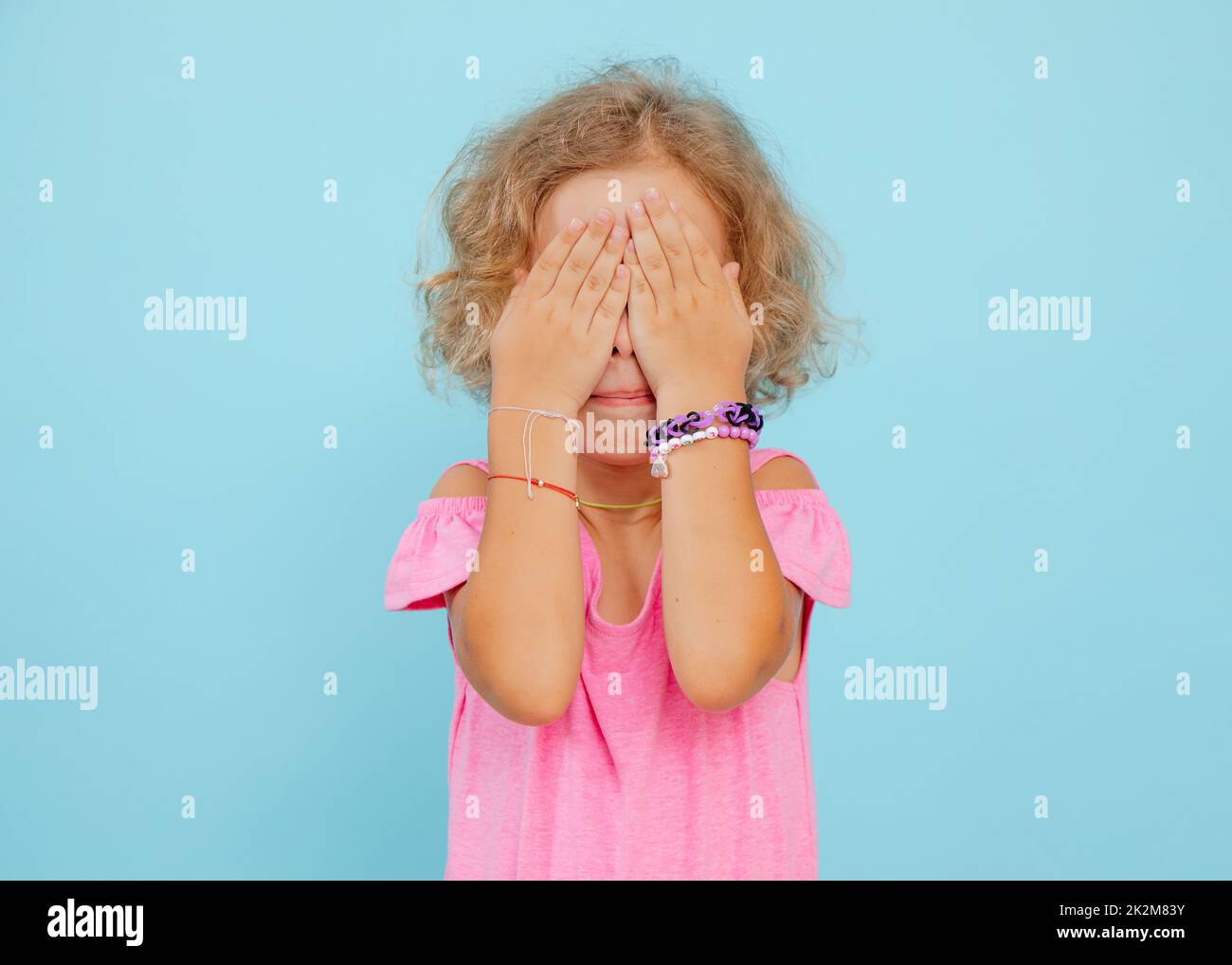 Portrait von verängstigten kleinen Mädchen, das die Augen mit Händen bedeckt, die das Gesicht auf blauem Hintergrund verbergen. Emotionen, Ängste, Studio. Stockfoto
