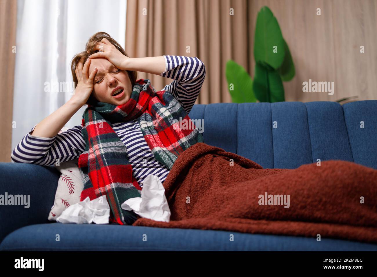 Junge Frau, die an einem Grippevirus erkrankt ist und unter starken Kopfschmerzen leidet, während sie auf der Couch liegt Stockfoto