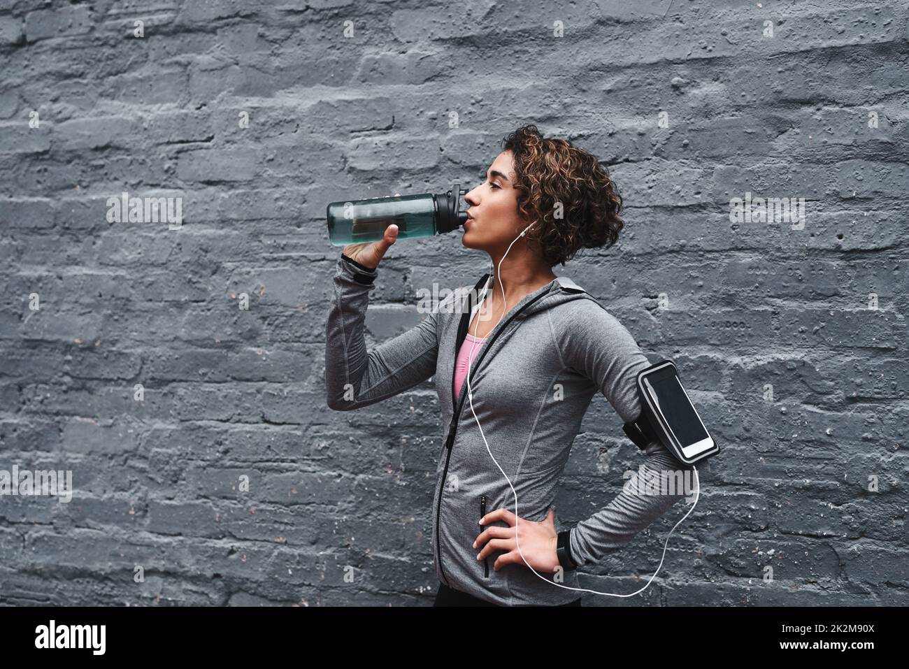 Hydrieren und ersetzen Sie diese Elektrolyte. Kurze Aufnahme einer attraktiven jungen Frau, die Musik hört und Wasser trinkt, nachdem sie draußen trainiert hat. Stockfoto