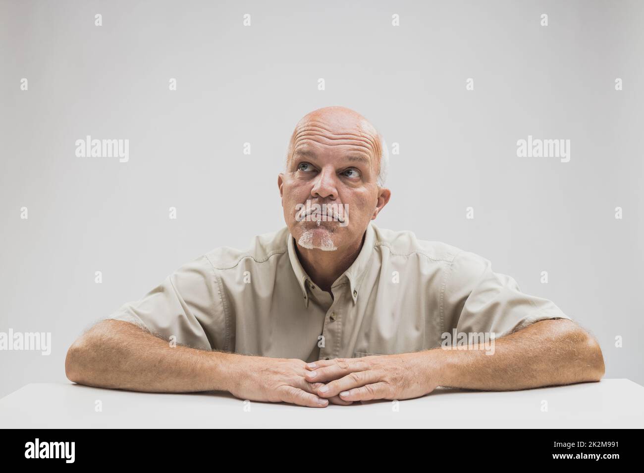Rücksichtsvoller, älterer, kahlköpfiger Mann, der an einem Tisch sitzt Stockfoto