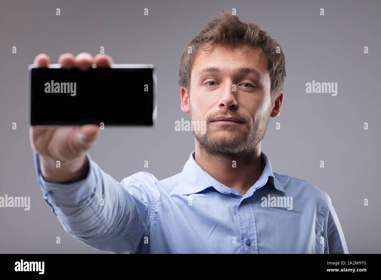 Ein junger bärtiger Mann hält ein Handy in der Hand Stockfoto