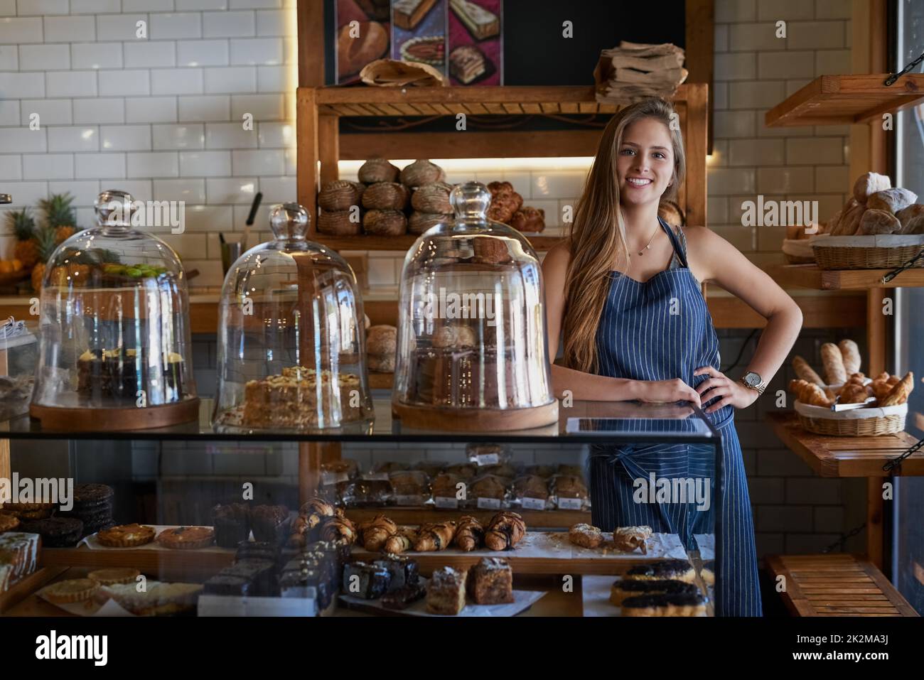 Alle unsere Leckereien werden perfekt gebacken. Porträt einer jungen Unternehmerin, die hinter dem Tresen ihrer Bäckerei steht. Stockfoto