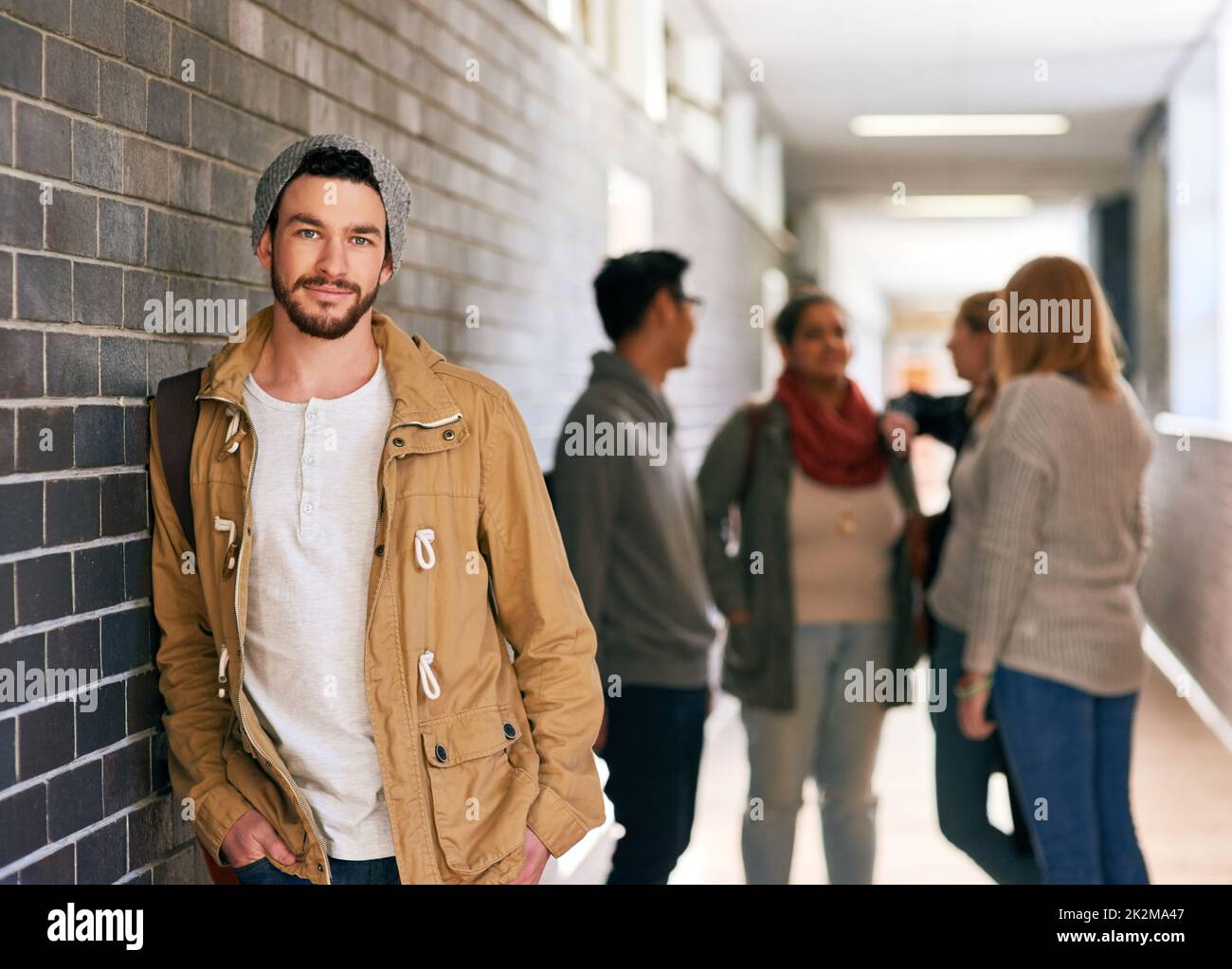 Cooler Typ auf dem Campus. Porträt eines jungen Studenten, der in einem Campus-Korridor mit seinen Klassenkameraden im Hintergrund steht. Stockfoto