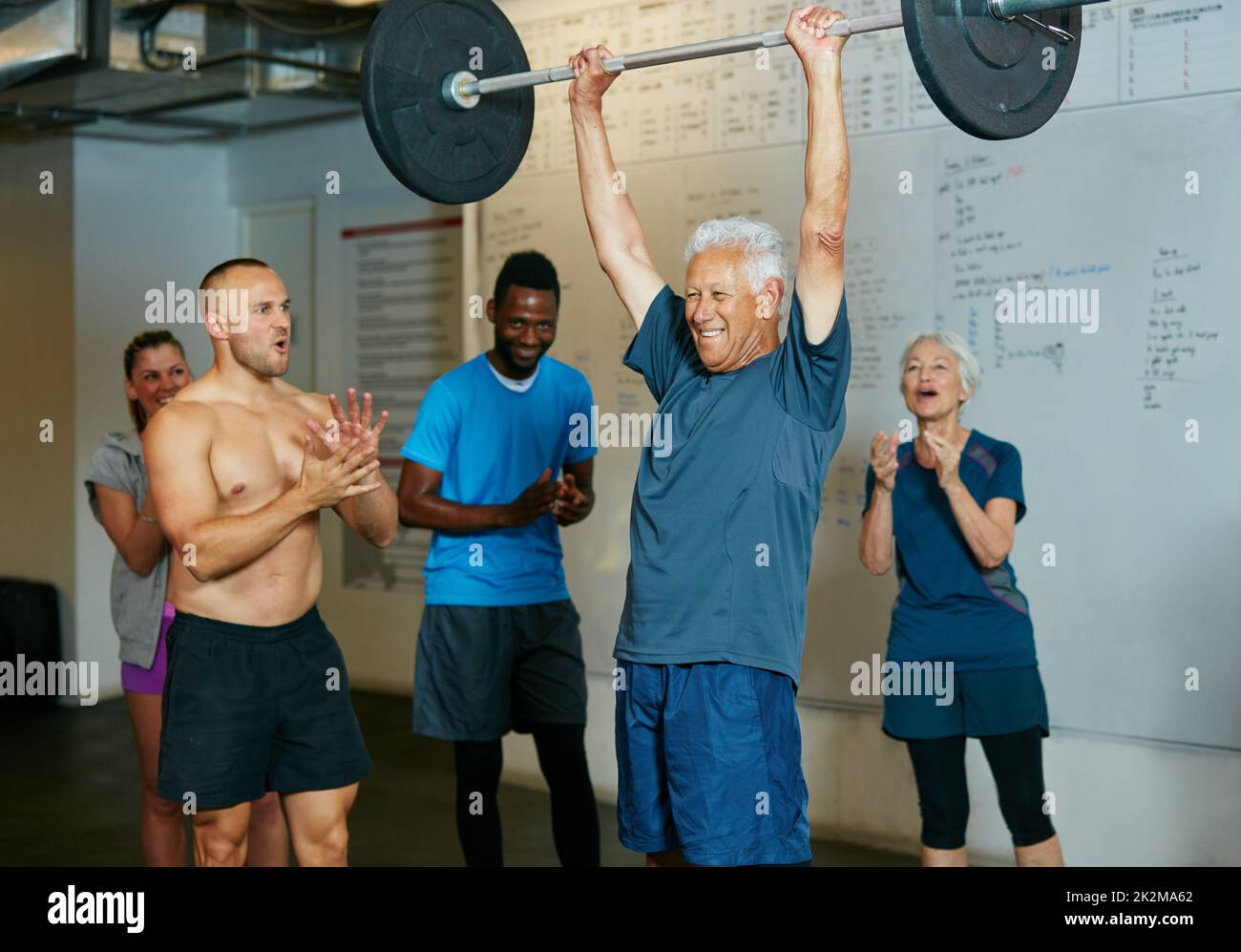 Unmöglich ist nichts. Aufnahme eines älteren Mannes, der Gewichte hebt, während eine Gruppe von Personen im Hintergrund zusehen. Stockfoto