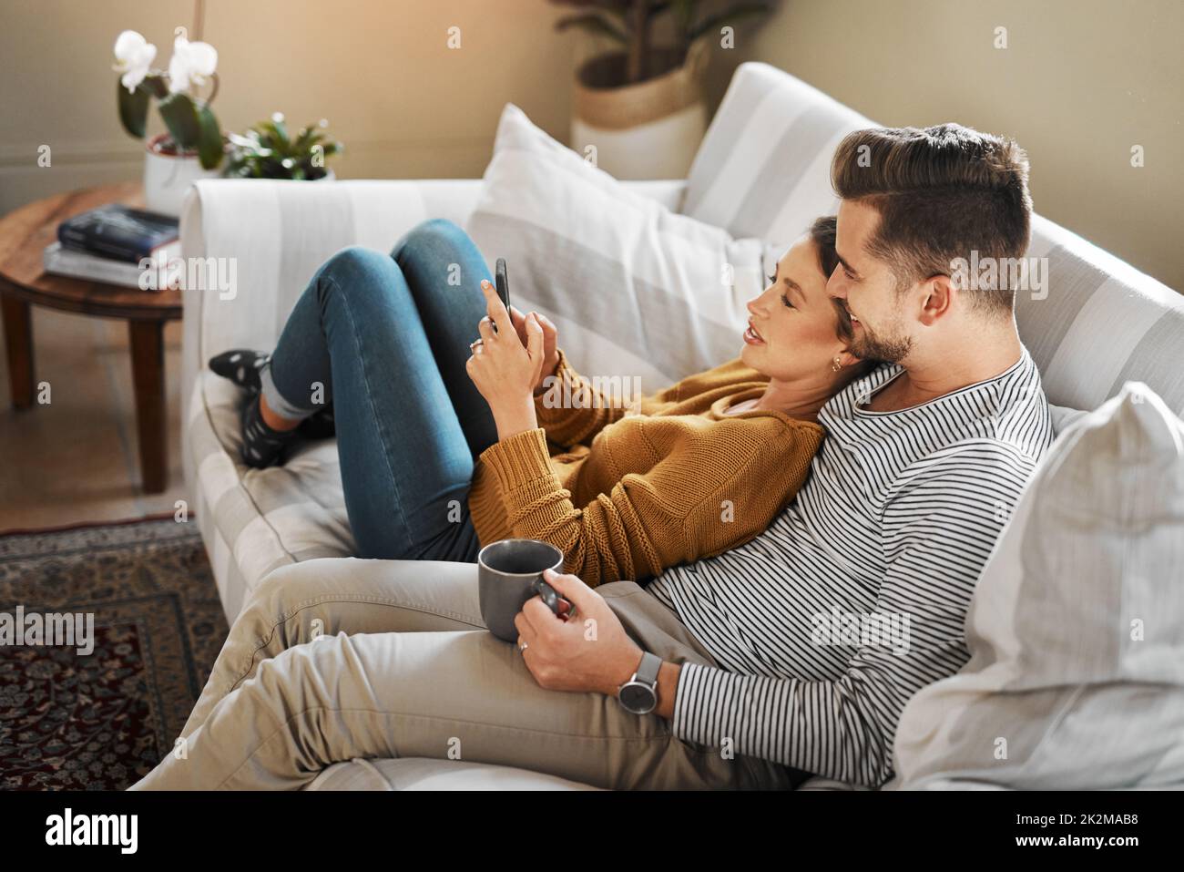 Sehen wir uns an, welche Sendungen in den sozialen Medien Trend sind. Aufnahme eines jungen Paares, das ein Mobiltelefon benutzt, während es sich auf dem Sofa zu Hause entspannt. Stockfoto