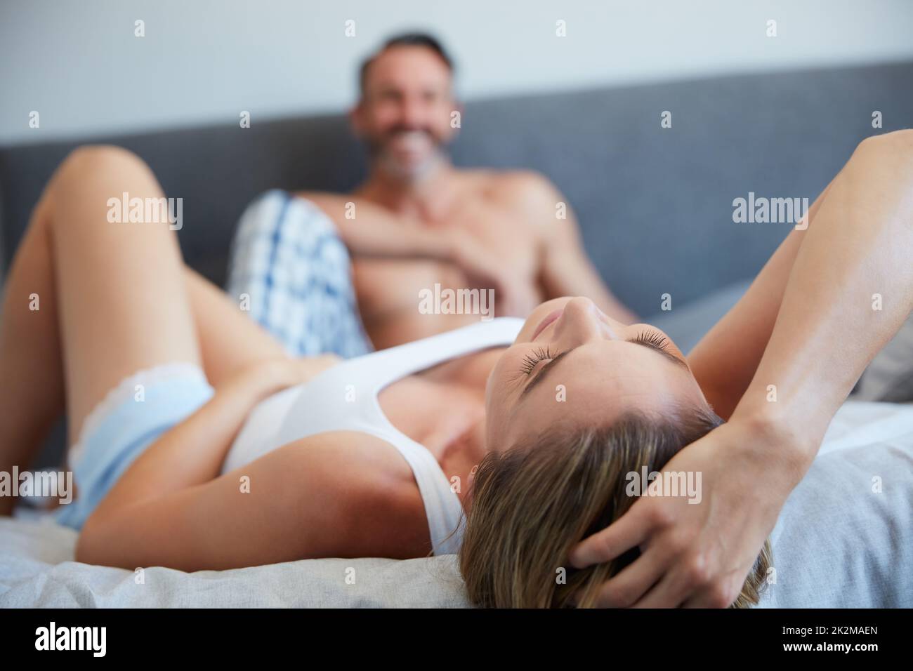 Teilen Sie sich ein Bett mit Glück. Aufnahme einer jungen Frau, die mit ihrem Mann im Hintergrund auf einem Bett liegt. Stockfoto