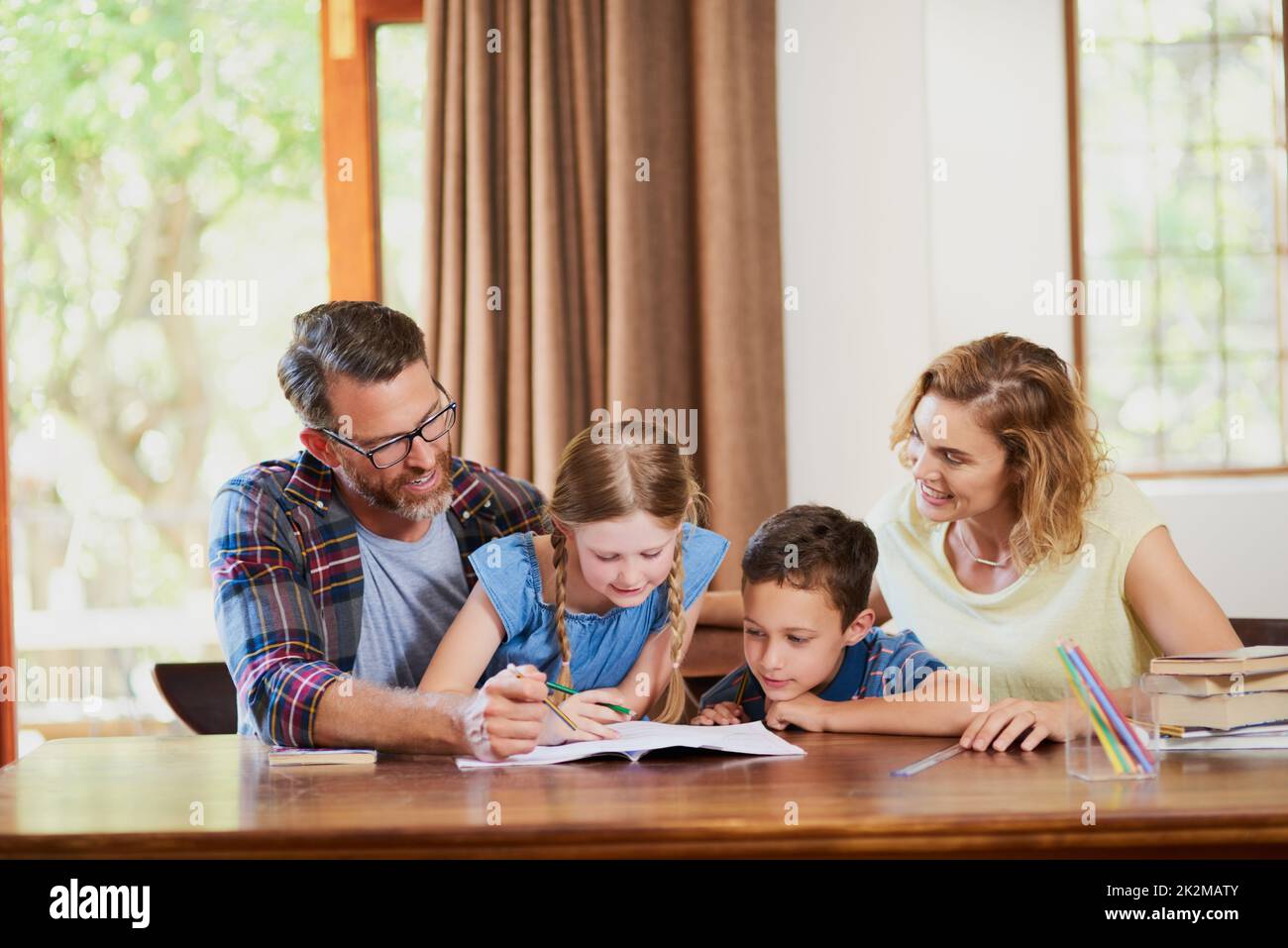 Wir alle sind hier, um bei den Hausaufgaben zu helfen. Eine kurze Aufnahme von zwei Eltern, die ihren entzückenden Kindern zu Hause bei der Schularbeit helfen. Stockfoto