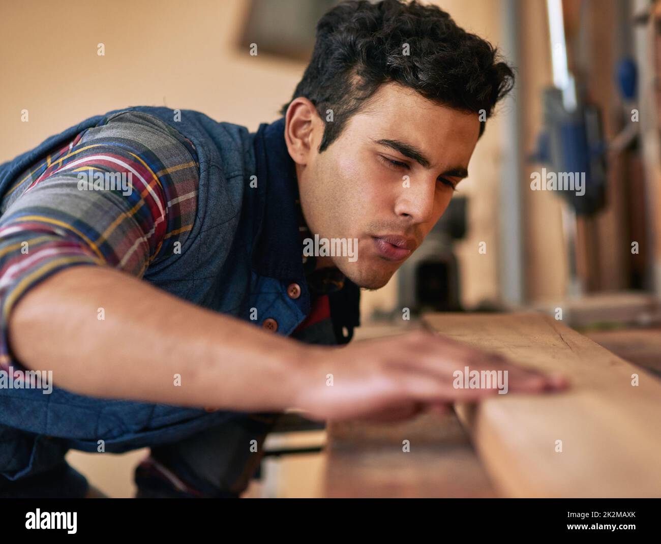 Er liebt es, es selbst zu tun. Aufnahme eines fokussierten Handwerkers, der ein Stück Holz während der Arbeit in seiner Werkstatt untersucht. Stockfoto