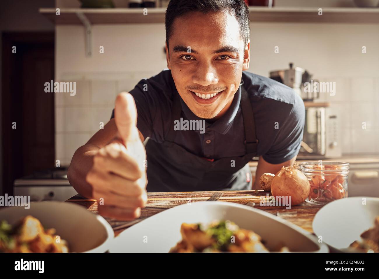 Das Essen war für einen König geeignet. Porträt eines jungen Mannes, der Daumen hoch zeigt, während er zu Hause ein köstliches Essen zubereitet. Stockfoto