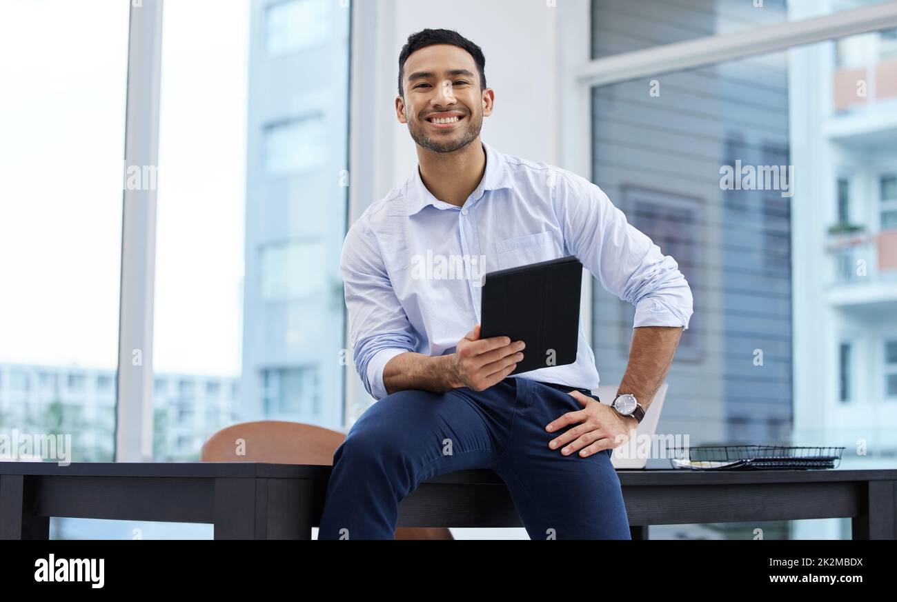 Mein Name wird weltweit in den Zimmern gesprochen. Aufnahme eines hübschen jungen Geschäftsmannes, der allein in seinem Büro sitzt und ein digitales Tablet in der Hand hält. Stockfoto