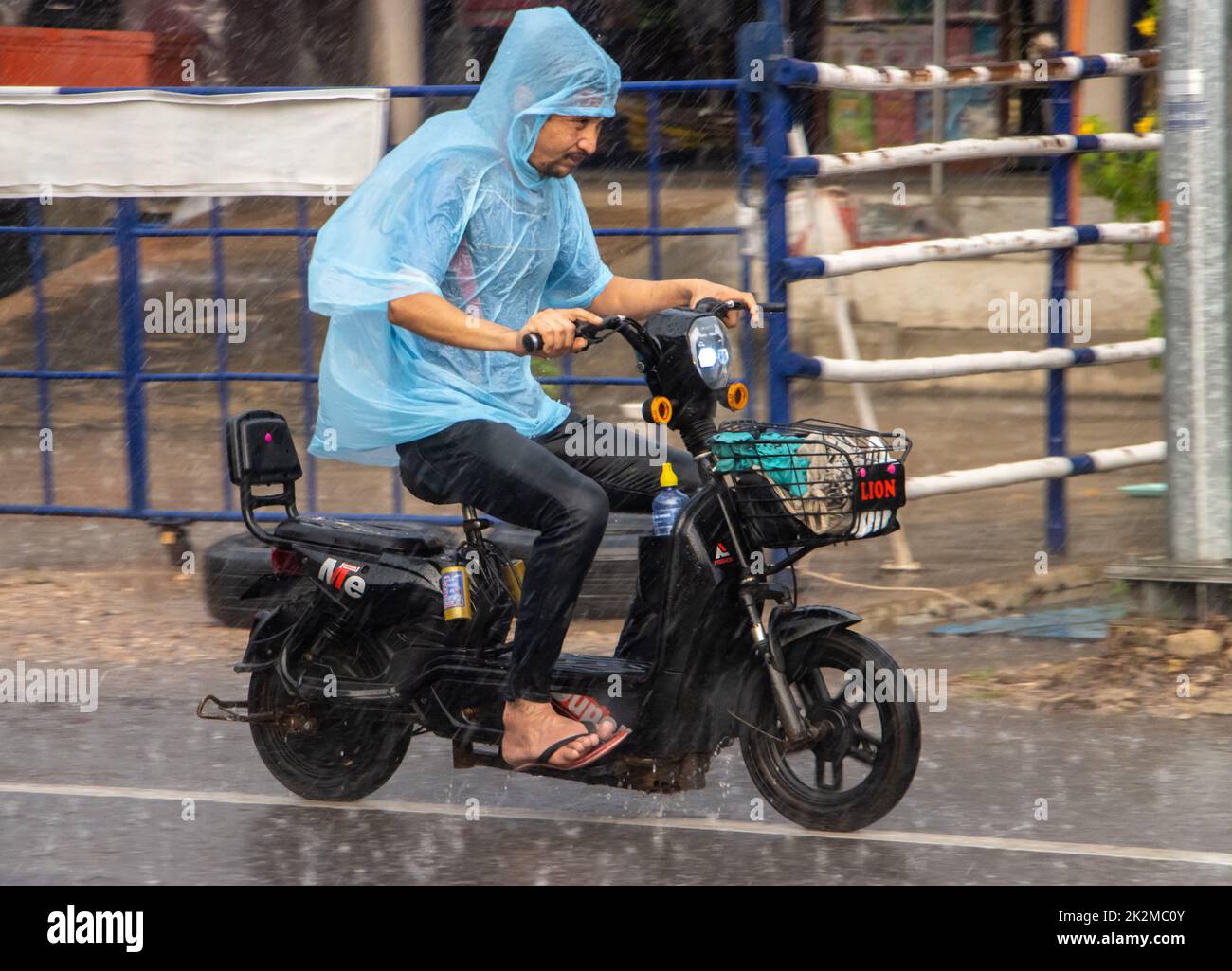 SAMUT PRAKAN, THAILAND, SEP 21 2022, Ein Mann im Regenmantel fährt bei starkem Regen mit einem Elektrofahrrad auf der Straße Stockfoto