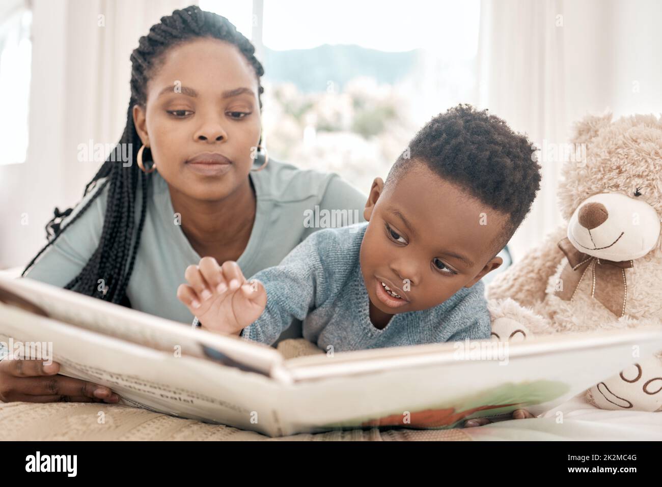 Lesen mit Mama. Ein kurzer Schuss eines entzückenden kleinen Jungen und seiner Mutter, die zu Hause ein Buch auf einem Bett lesen. Stockfoto
