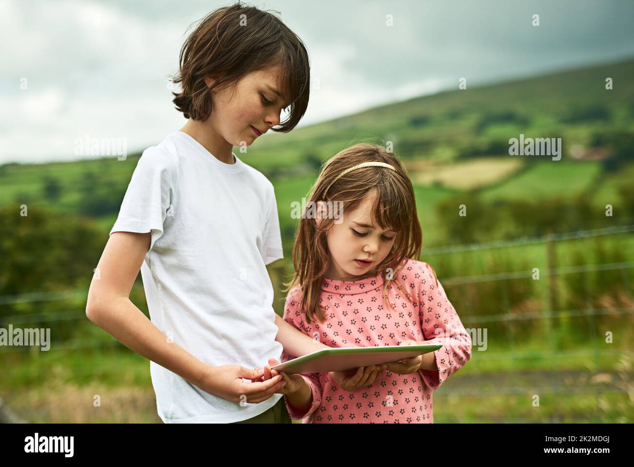 Die Wunder der digitalen Welt teilen. Aufnahme von zwei kleinen Geschwistern mit einem digitalen Tablet im Freien. Stockfoto
