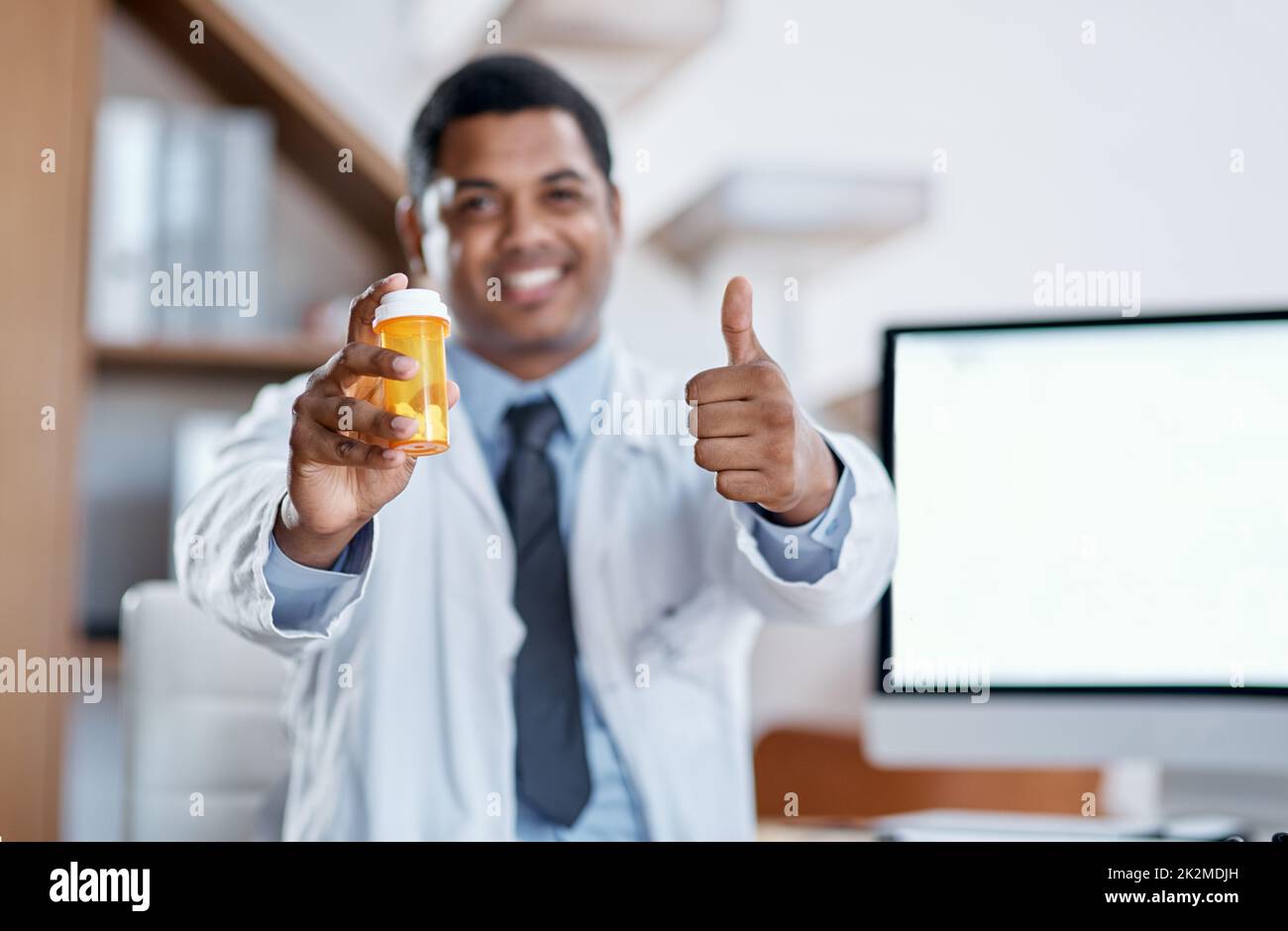 Er schreibt nur das Beste vor. Porträt eines jungen Arztes, der eine Flasche Pillen hält und in seinem Büro Daumen nach oben zeigt. Stockfoto