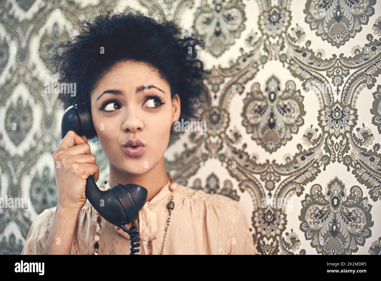 Oh, wirklich. Studioaufnahme einer jungen Frau in einem Vintage-Outfit, die auf einem altmodischen Telefon spricht. Stockfoto