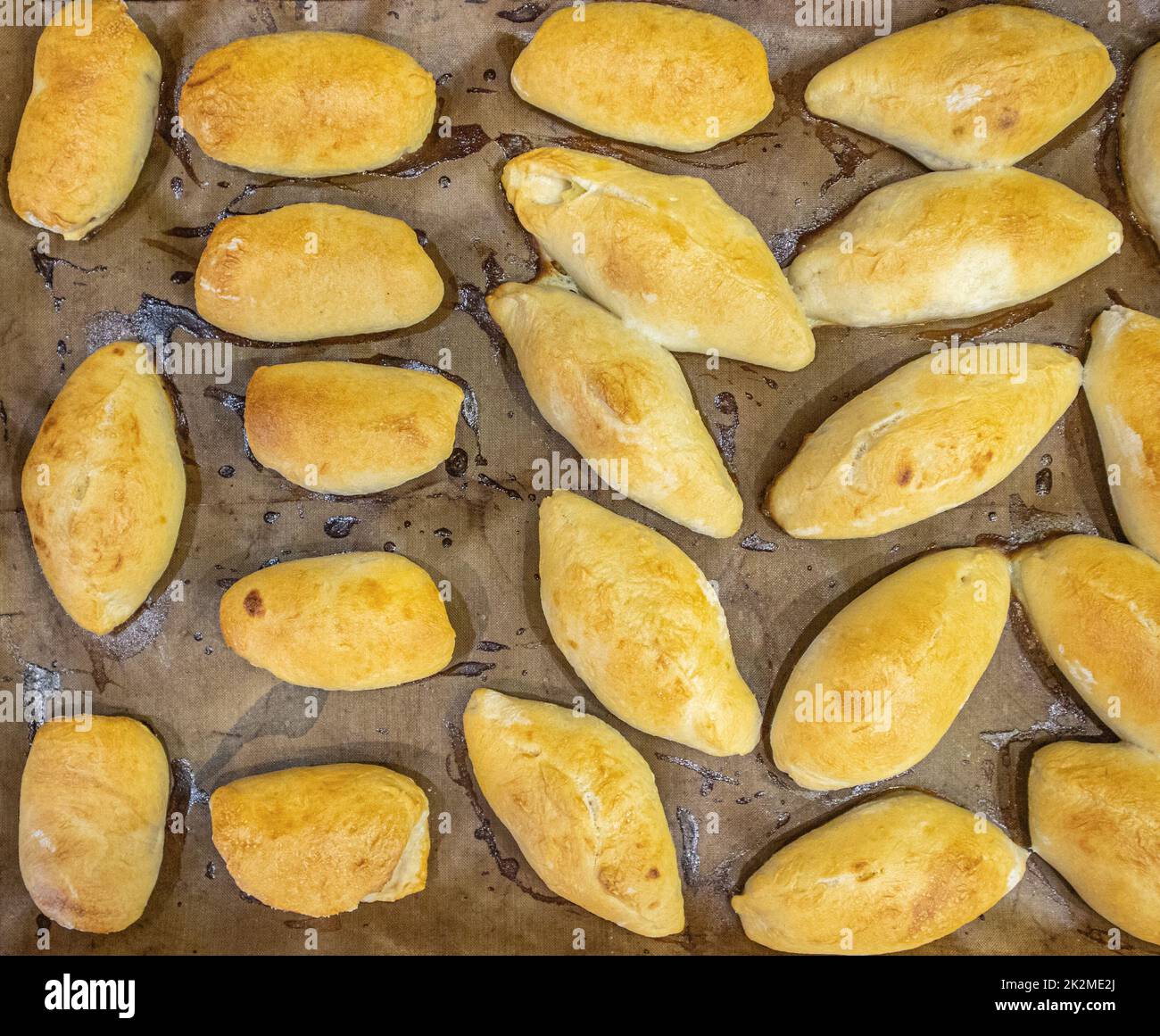 Legen Sie die frisch gebackenen Pasteten mit der Füllung auf ein mit Backpapier bedecktes Backblech. Köstliche frische hausgemachte Backwaren aus dem Ofen. Draufsicht Stockfoto