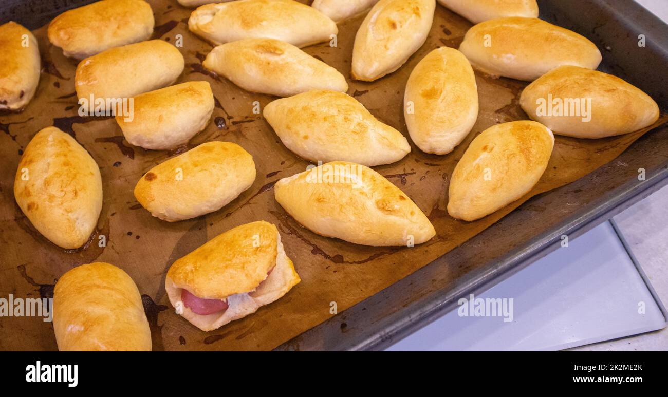 Legen Sie die frisch gebackenen Pasteten mit der Füllung auf ein mit Backpapier bedecktes Backblech. Köstliche frische hausgemachte Backwaren aus dem Ofen. Draufsicht Stockfoto