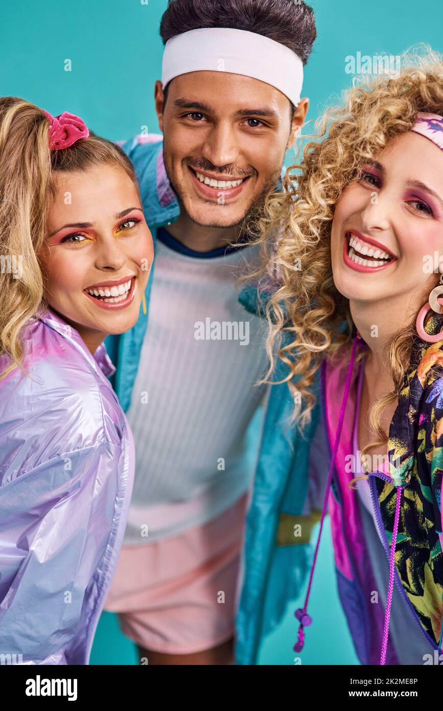 Bereit für 80s Spaß. Aufnahme von drei jungen Menschen, die in 80s Kleidungsstücken vor blauem Hintergrund posieren. Stockfoto