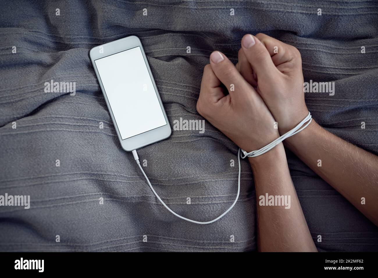 Befreien Sie sich von den Technologieketten. Ausgeschnittene Aufnahme einer nicht erkennbaren Person, die an einem Handy-Ladekabel gebunden ist. Stockfoto