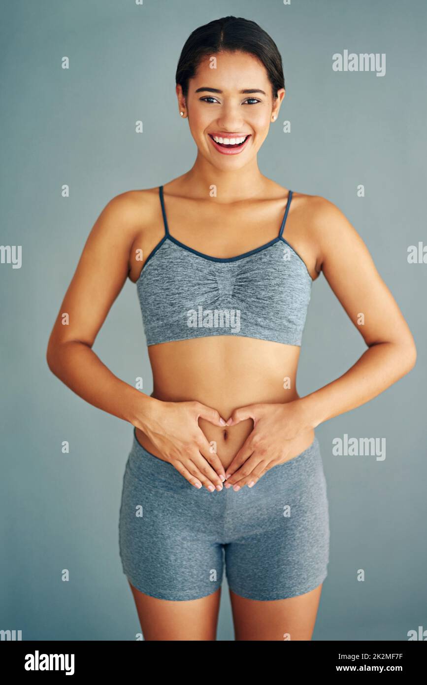 Liebe deinen Körper. Eine kleine Aufnahme einer jungen Frau, die eine Herzform auf ihrem Bauch formt. Stockfoto