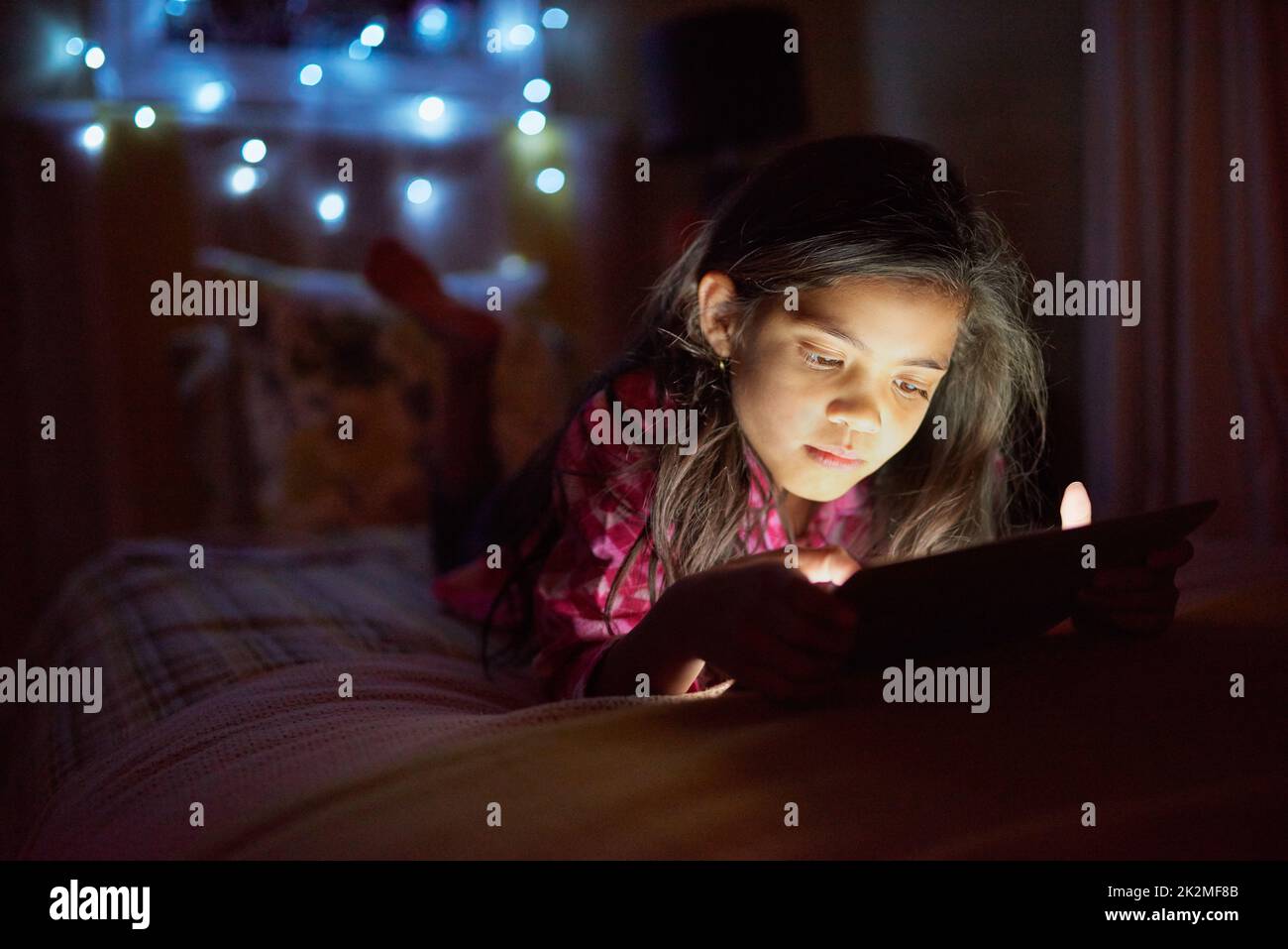 Nur noch eine Geschichte. Aufnahme eines kleinen Mädchens mit einem digitalen Tablet spät in der Nacht in ihrem Schlafzimmer. Stockfoto