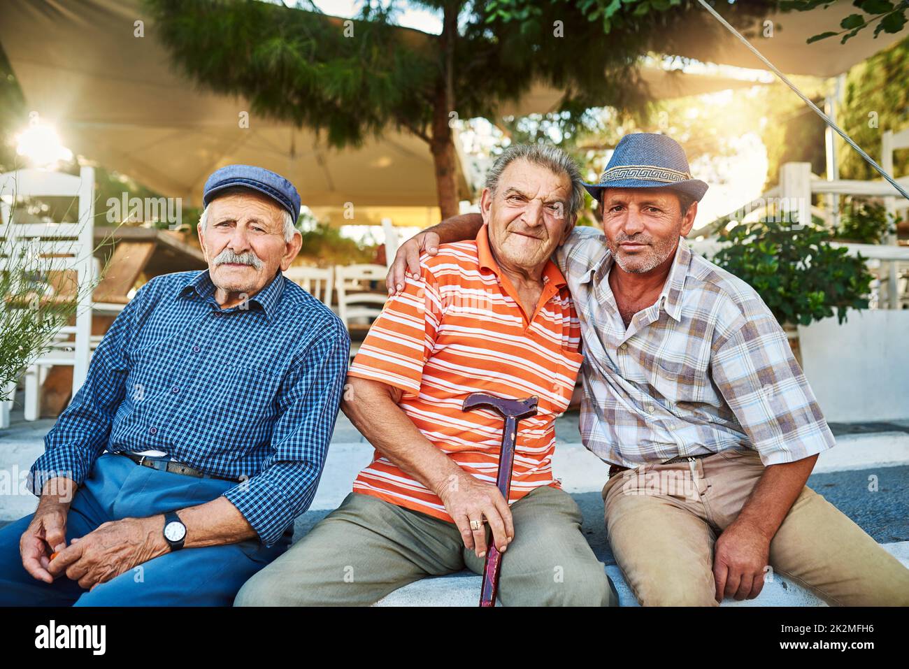 Sie sind Freunde, seit sie Kinder waren. Porträt einer Gruppe von fröhlichen älteren Männern, die zusammen sitzen, während sie draußen in die Kamera blicken. Stockfoto