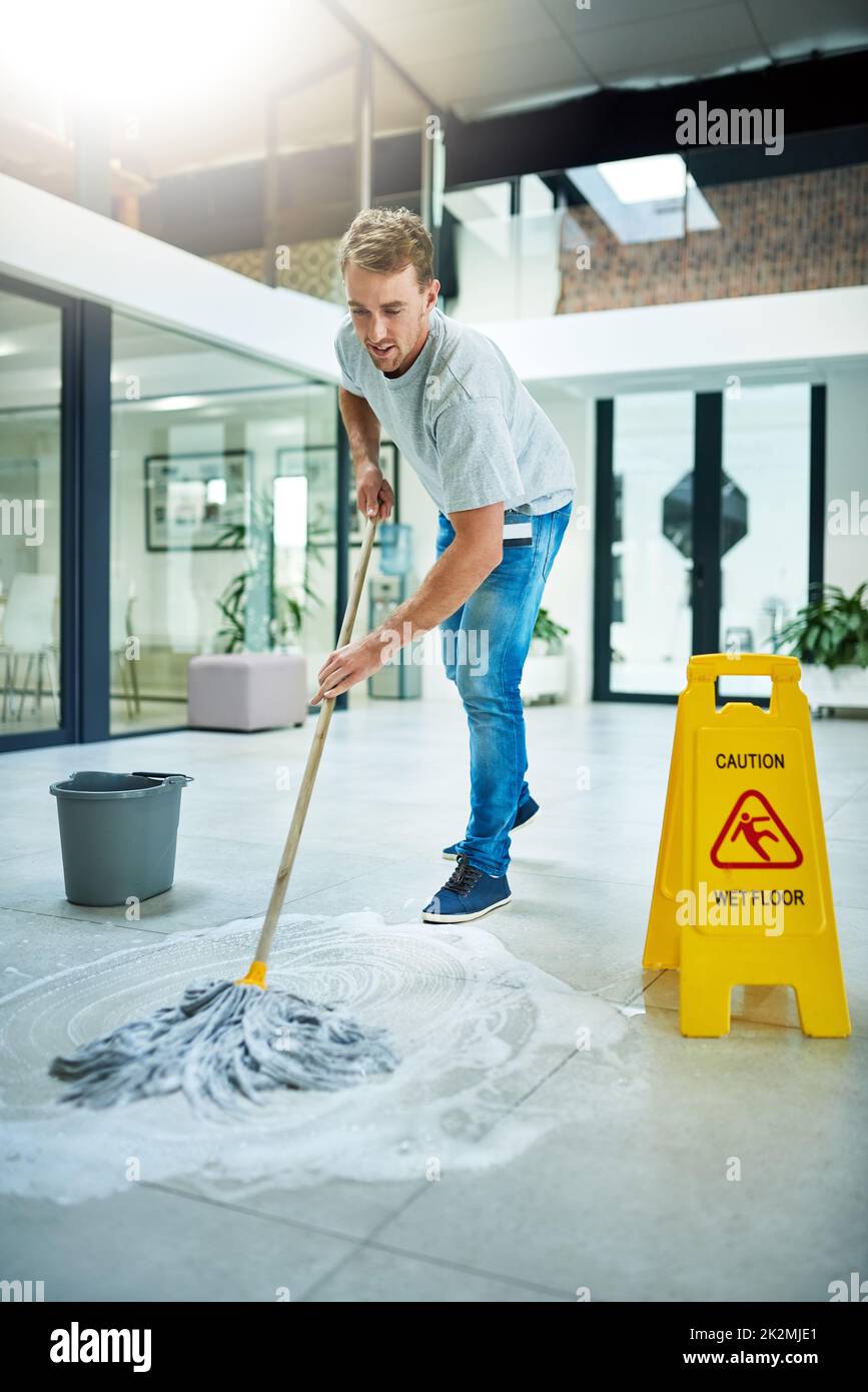 Etwas Ellenbogenfett geben. Aufnahme eines jungen Mannes, der die Büroetage wischt. Stockfoto