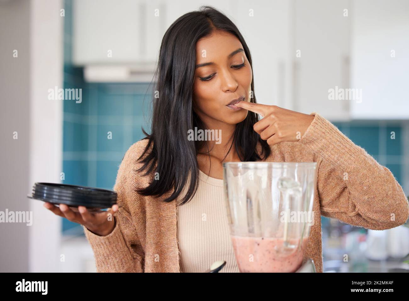 Es schmeckt so lecker, wie es aussieht. Aufnahme einer jungen Frau, die zu Hause einen gesunden Smoothie vorbereitet. Stockfoto