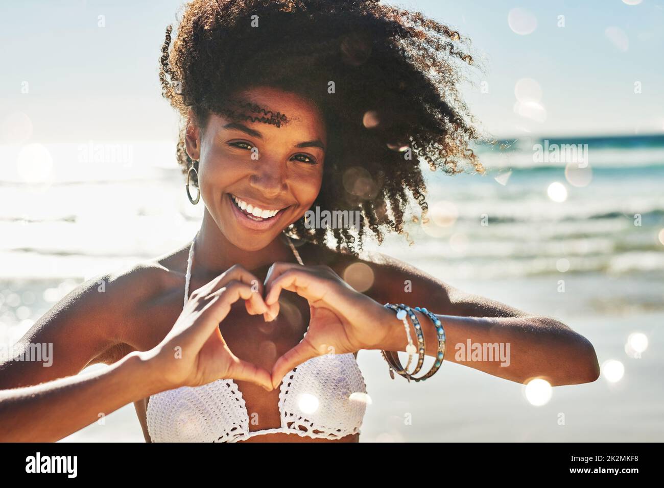 Mein Herz gehört zum Sommer. Porträt einer schönen jungen Frau, die mit ihren Händen am Strand eine herzförmige Geste macht. Stockfoto