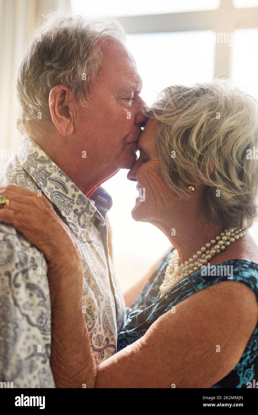 Die Sprache der Liebe braucht keine Worte. Aufnahme eines älteren Mannes, der zu Hause zärtlich seine Frau auf die Stirn küsst. Stockfoto