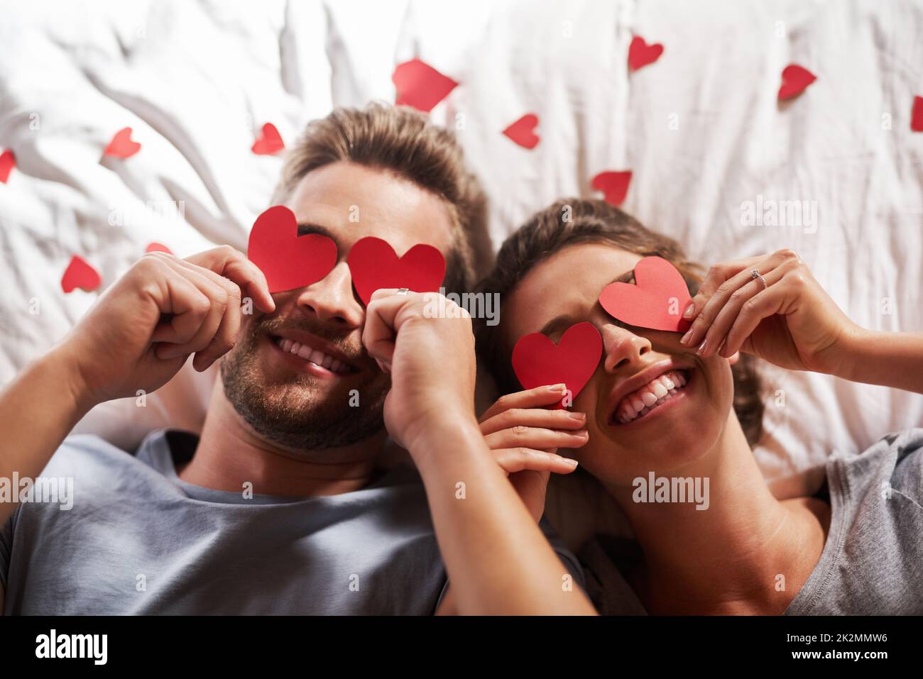 Liebe und Glück in Sicht. Aufnahme eines liebevollen jungen Paares, das im Schlafzimmer zu Hause ihre Augen mit Herzformen bedeckt. Stockfoto