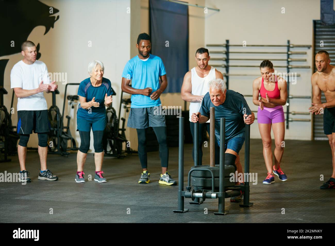 Ihn anfeuern. Ganzkörperaufnahme einer Gruppe von Leuten, die im Fitnessstudio einen älteren Mann anfeuern. Stockfoto