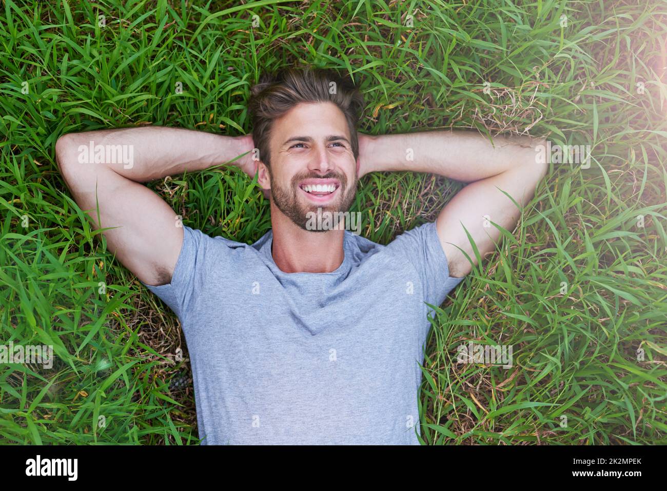 Auf der anderen Seite ist das Gras grüner. Hochwinkelige Aufnahme eines jungen Mannes, der auf dem Gras mit den Händen hinter dem Kopf liegt. Stockfoto