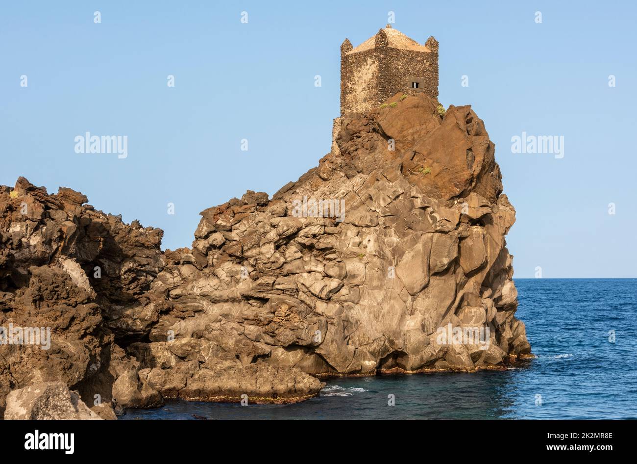 Ein mittelalterlicher Wachturm, der hoch auf einem Ausbiss vulkanischer Lava mit Blick auf das Ionische Meer thront, in der Nähe des kleinen Dorfes Santa Tecla, Acireale, Sizilien Stockfoto