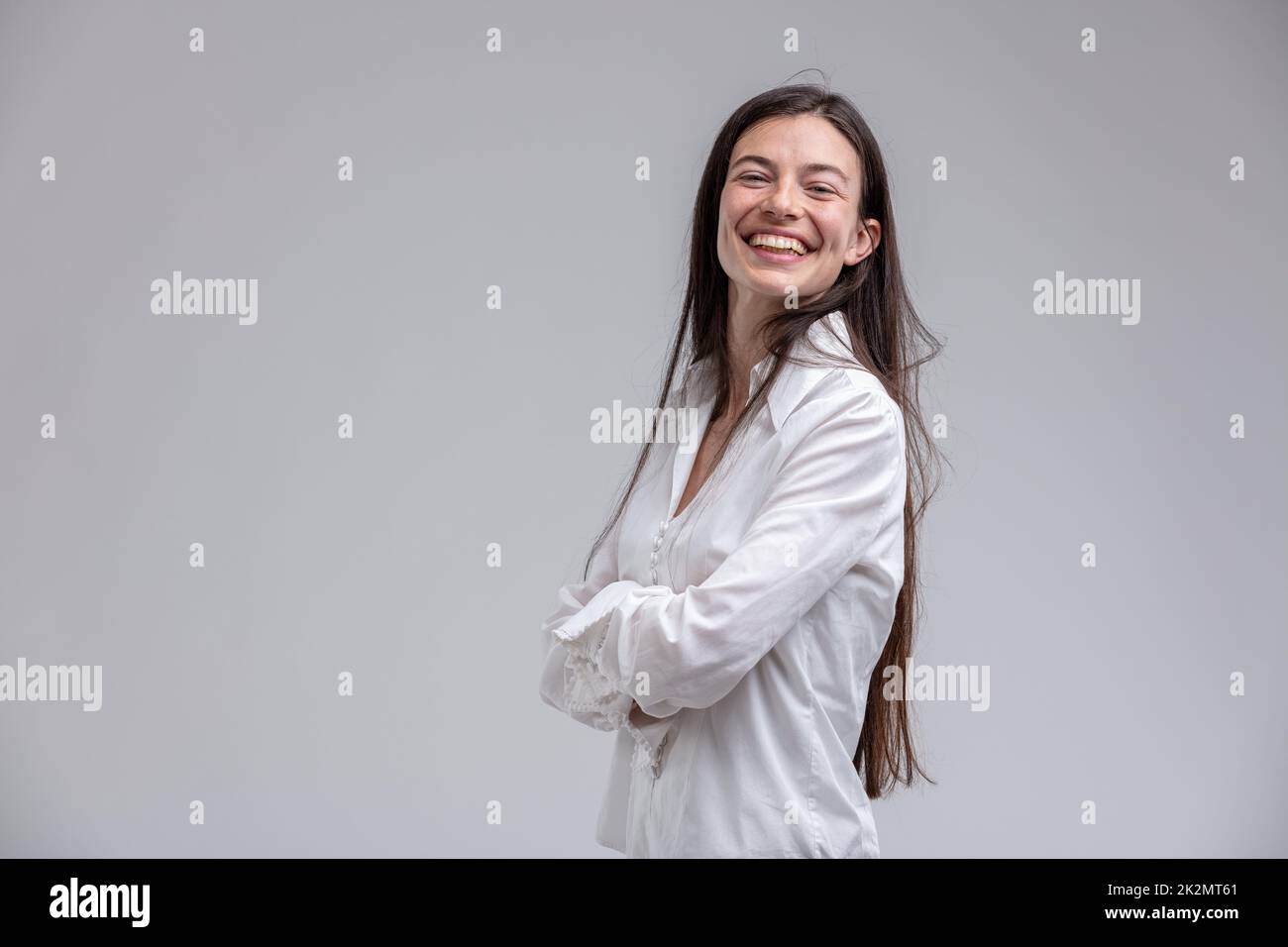 Langhaarige, fröhliche Frau mit gekreuzten Armen Stockfoto
